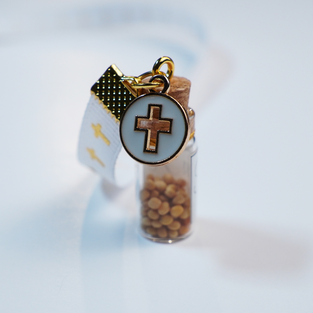 Separador de liston blanco con cruces doradas, borla, coldije y frasco con semillas de mostaza